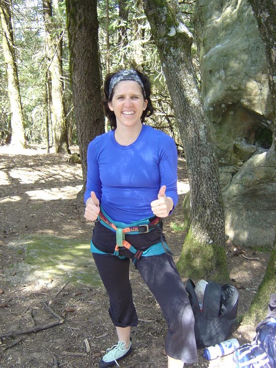 Claudia in a climbing harness giving two thumbs up in a forest