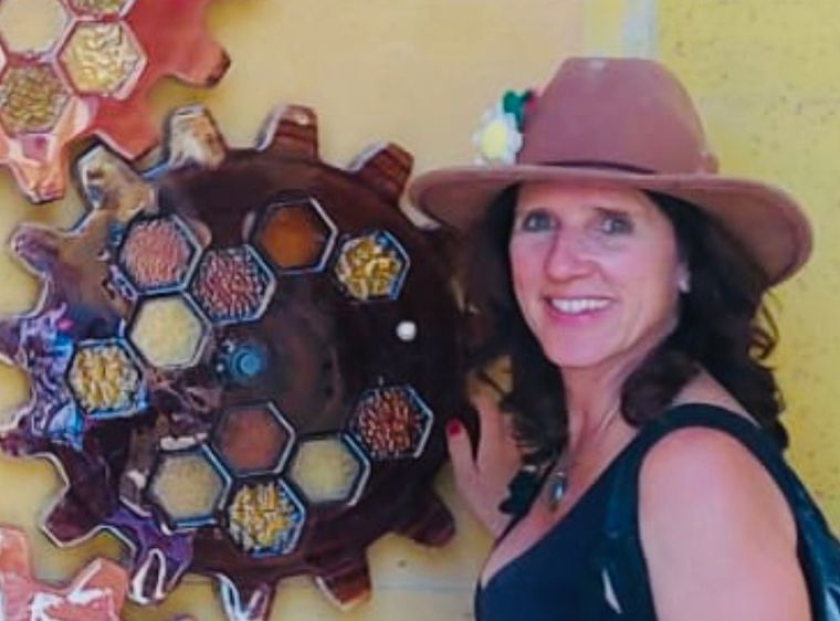 Claudia in a brown fedora beside a gear-shaped mosaic on a yellow wall
