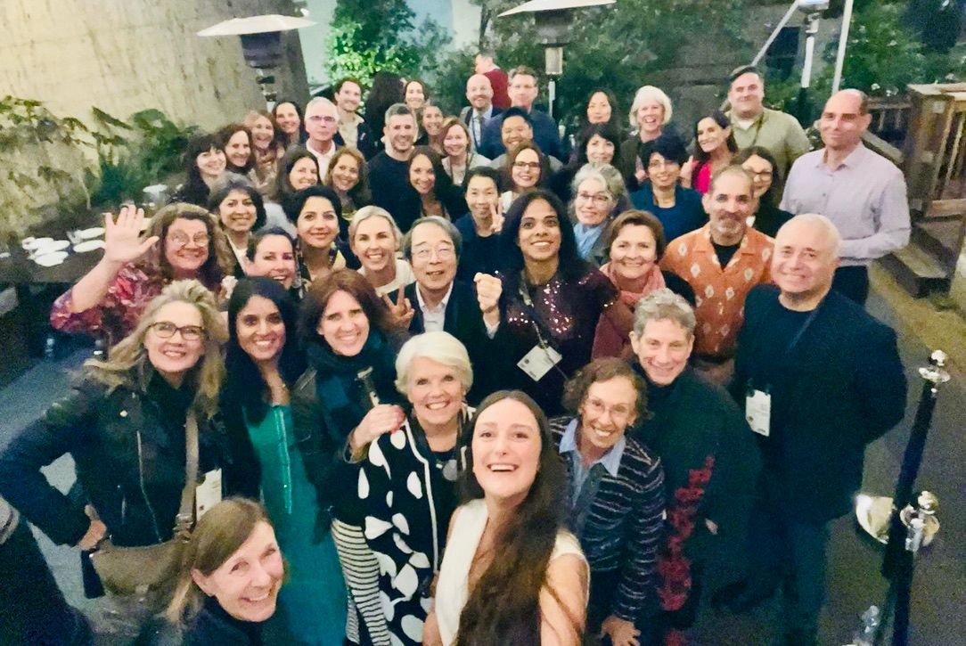 A large group squeezed together for a selfie at an evening event, many wearing name badges