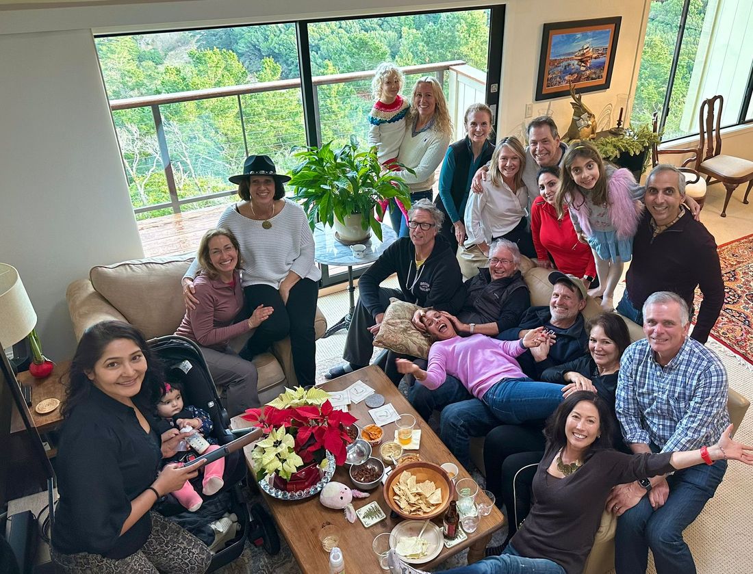 A big group of friends and their children crowded into a living room around a table of snacks and poinsettias