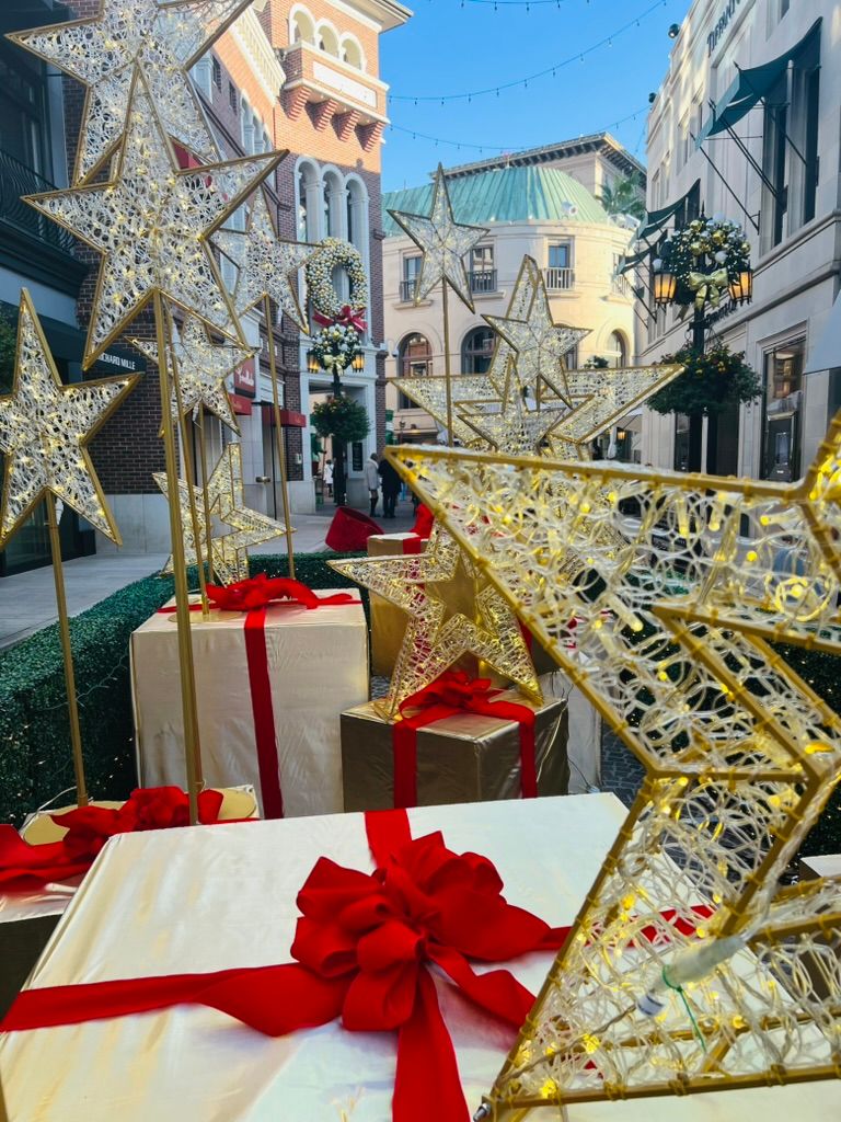 Giant gift boxes with red velvet bows under gold light-up stars on a decorated shopping street