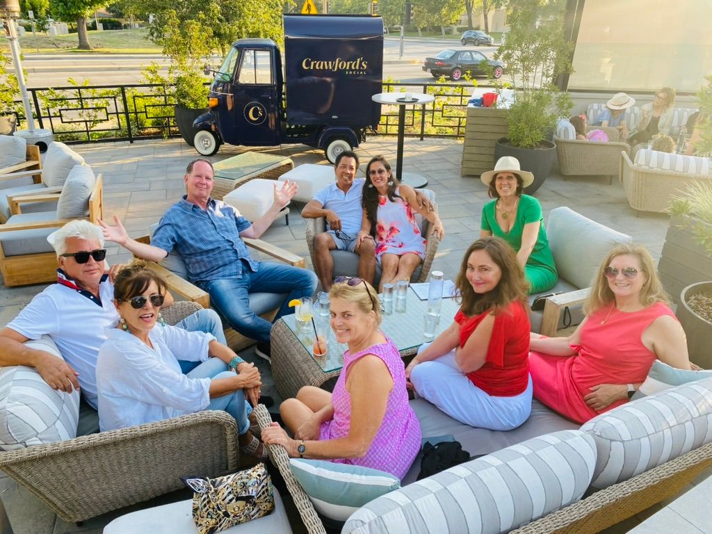 Claudia in a green dress and sun hat with a group of friends on wicker sofas on a sunny patio